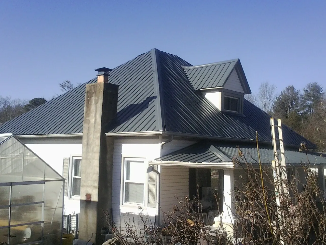Dark blue standing seam metal roof on a white farmhouse with dormer — Slate & Tile Roof Repair by Roofing Brothers in Bartonsville