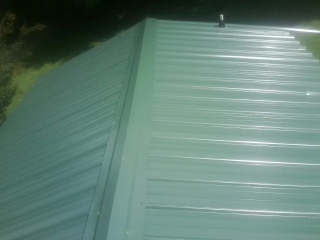 New green metal panels meeting at the ridge of a roof — Flat Roof Repair work by our crew in Bartonsville