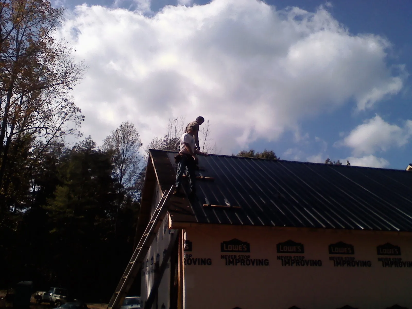 Roofer fastening dark metal panels high against a cloudy sky, from a Roof Inspection job in Bartonsville