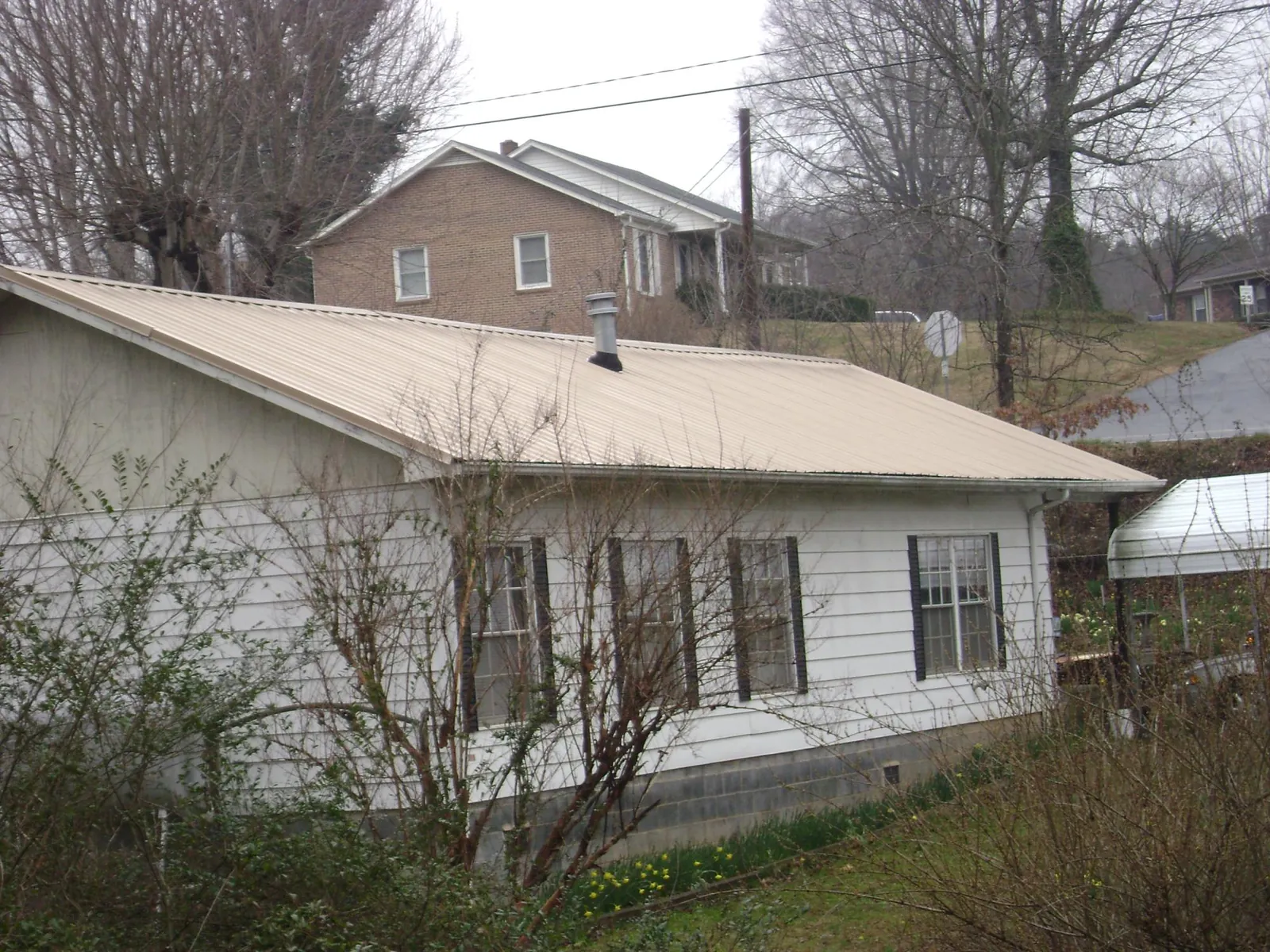 Tan metal roof on a white sided house set into a hillside — Commercial Roofing by Roofing Brothers in Bartonsville